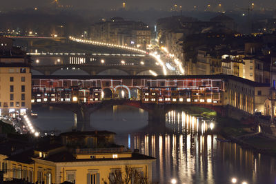 Illuminated bridge over river by buildings in city at night