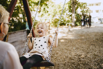 Happy girl laughing while playing on swing with grandmother at park