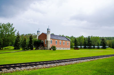 Railroad tracks by grassy field against built structure at fort edmonton park