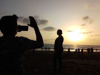 Silhouette people photographing sea against sky during sunset