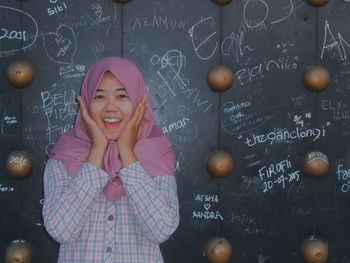 Portrait of surprised teenage girl standing against blackboard in classroom