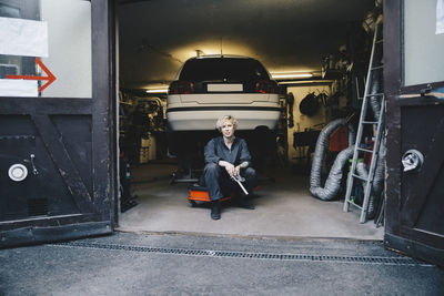 Female mechanic sitting by car at entrance of auto repair shop