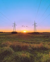 Electricity pylon on field against sky during sunset