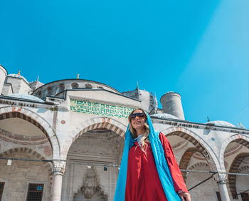 Low angle view of woman standing outside mosque against clear blue sky