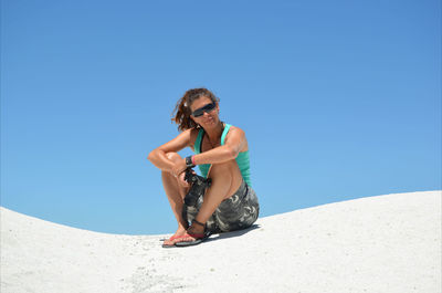 Portrait of woman sitting on sand against clear blue sky