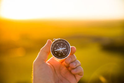 A hand holding a compass in a natural landscape at sunset