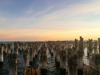 Scenic view of  wooden posts at sea against cloudy sky