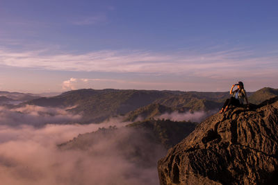 Woman sitting on mountain against sky during sunset