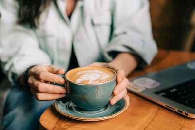 Close-up coffee mug with cappuccino art in female hands.