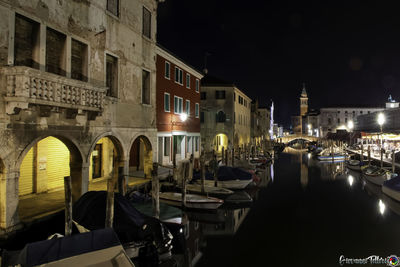 Boats moored in canal amidst buildings in city at night