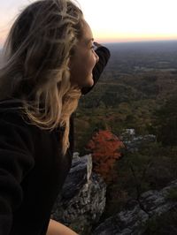 Side view of young woman looking at rocks against sky