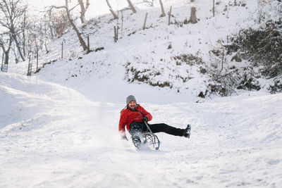 Happy man riding sleigh on snow covered hill during winter