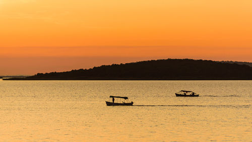 Silhouette boats in sea against orange sky