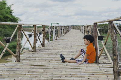 Side view of boy sitting on railing against sky