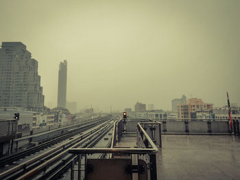 Railroad tracks by buildings in city against sky