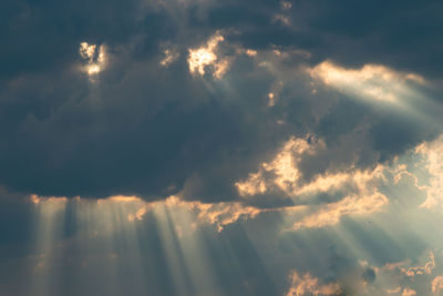 Low angle view of sunlight streaming through clouds