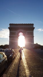 Man standing on road leading towards arc de triomphe during sunset