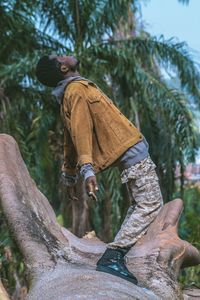 Side view of man standing on tree trunk