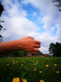 Midsection of person hand on grassy field against cloudy sky