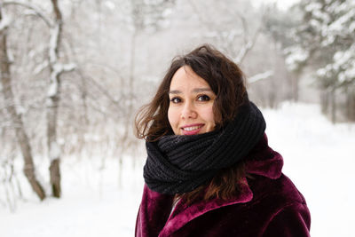 Smiling woman with long brown hair in a coat from faux fur on a background of winter forest.