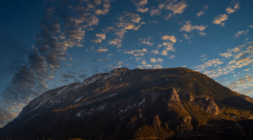 Low angle view of rocks on mountain against cloudy sky