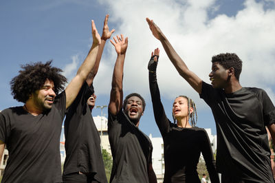 Side view of friends gesturing against sky