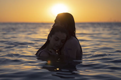 Woman swimming in sea against sky during sunset