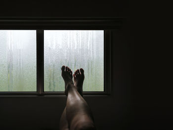 Low section of woman leaning on window sill in darkroom at home