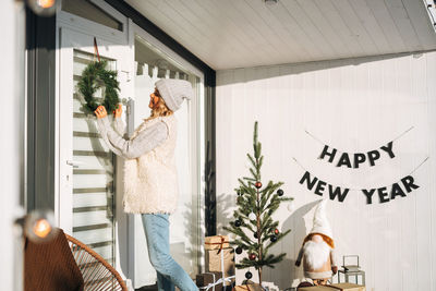 Smiling woman with blonde hair in winter clothes decorating her country house in christmas time