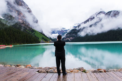 Rear view of man standing on lake against mountain