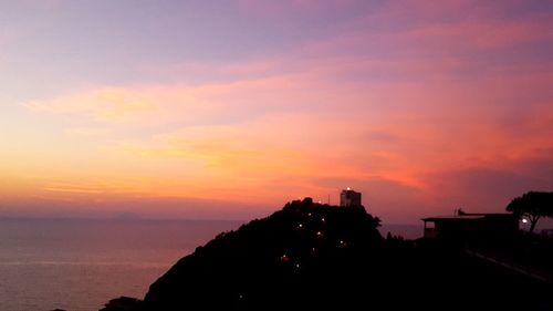 Silhouette buildings by sea against romantic sky at sunset