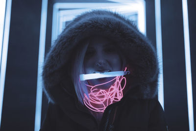 Woman in hooded clothing carrying equipment in mouth standing against illuminated lights