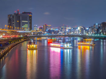 Illuminated bridge over river in city at night