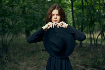 Portrait of young woman standing against trees