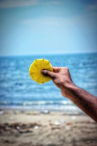 Close-up of hand holding yellow leaf on beach