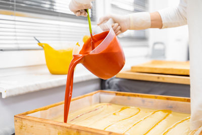 Close-up of hand pouring red liquid in wooden tray
