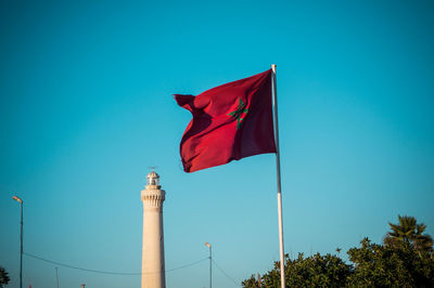 Low angle view of moroccan flag and lighthouse against blue sky. casablanca, morocco