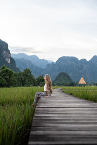 Rear view of man walking on boardwalk against sky