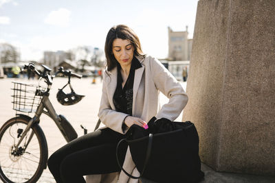 Businesswoman searching in purse while sitting by bicycle