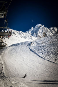 A boarder cutting down a red slope in les arcs, with the moon in the sky