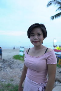 Portrait of smiling woman standing on beach against sky