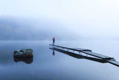 Man on pier in lake in morning fog