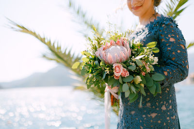 Midsection of woman standing by flowering plant in sea