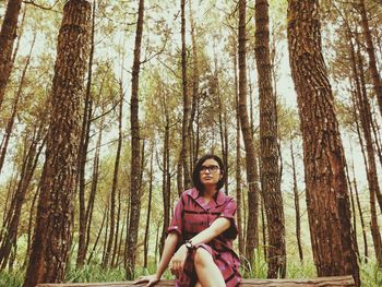 Beautiful woman sitting on log amidst trees in forest