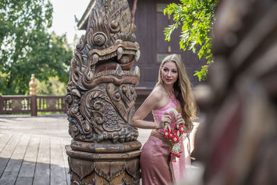 Portrait of smiling young woman outside temple against building