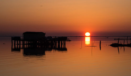 Silhouette wooden posts in sea against orange sky