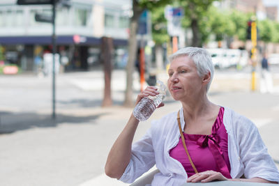 An aged woman with bob cut drink water from plastic bottle at the cafe table