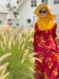 Woman standing on field wearing a stylish red dress with hat during summer