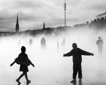 Silhouette people standing on street in city against cloudy sky