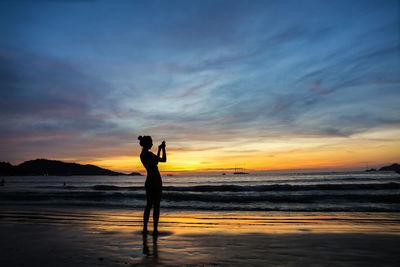 Silhouette woman standing on beach against sky during sunset